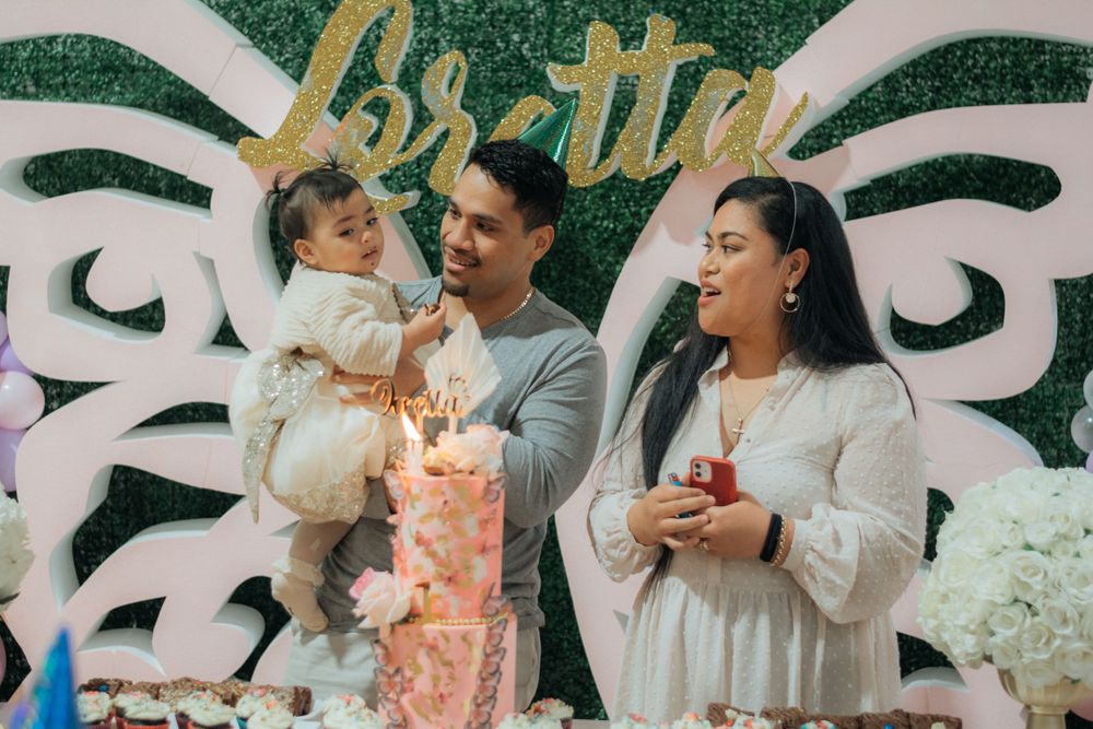 Family of three celebrate baby Loretta's first birthday with a floral cake and green backdrop.