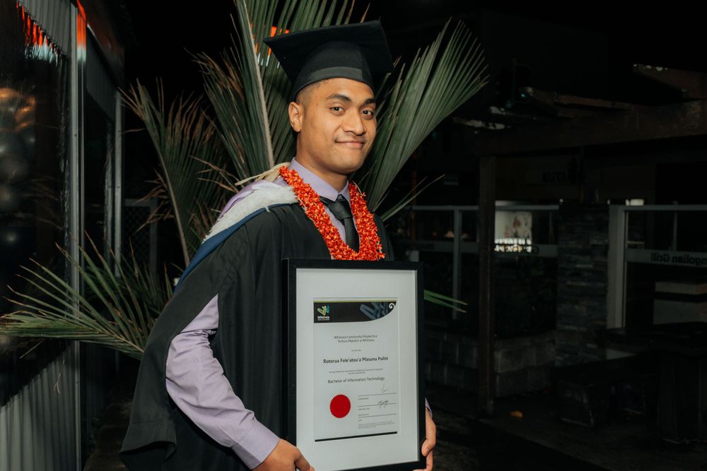 Proud graduate in cap and gown holding framed diploma certificate at graduation ceremony.