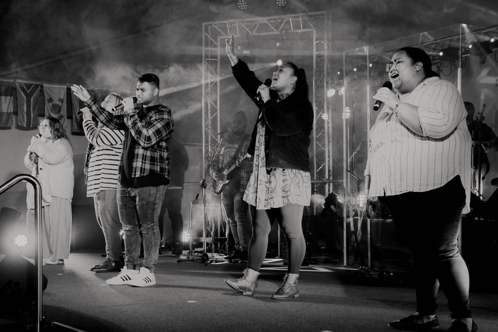 Black and white photo of group performing on stage with dramatic lighting and fog effects.