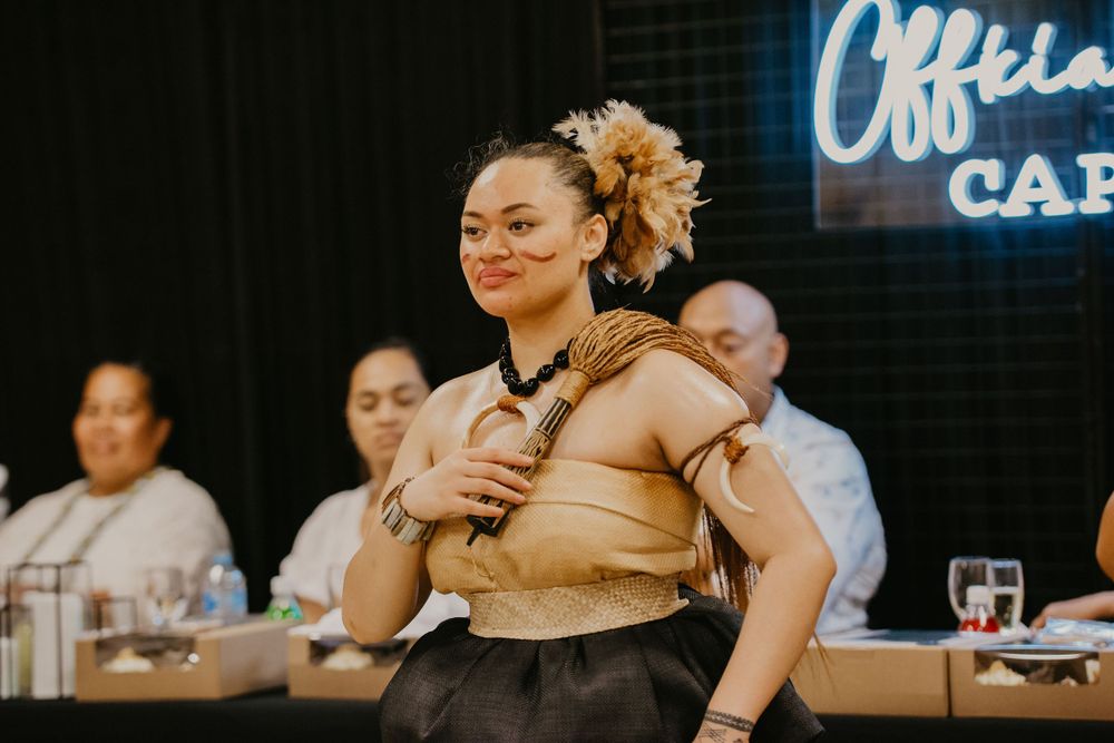 Young woman in traditional Polynesian gold costume performing cultural dance at event.