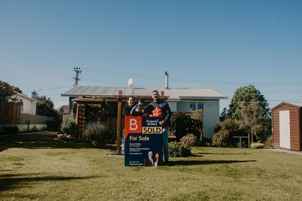 Happy couple jump for joy in front of a sold real estate sign outside their new home.