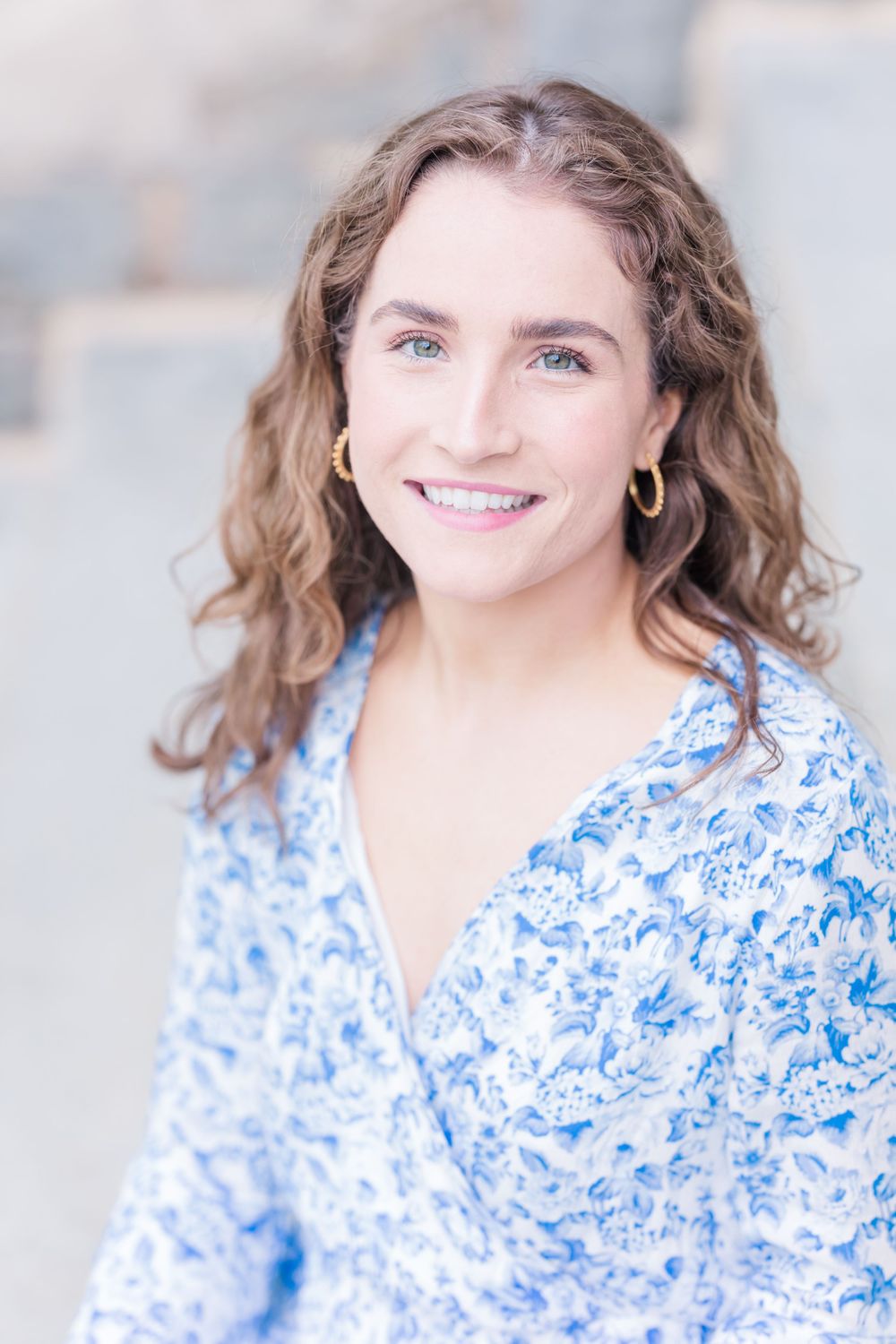 Portrait of woman wearing blue and white floral dress with gold hoop earrings.