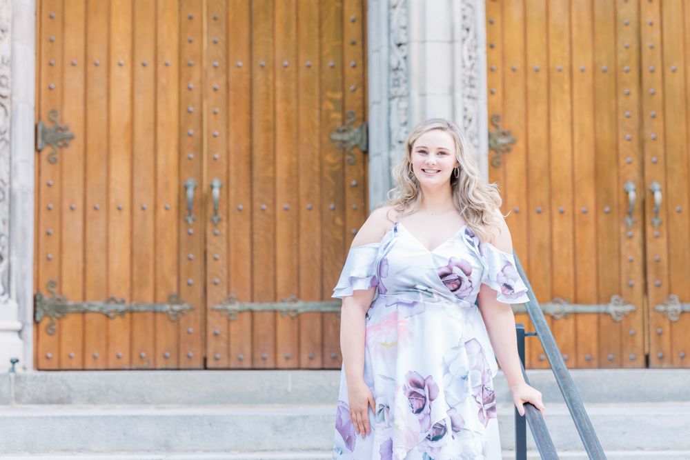 A person in a floral lavender dress poses in front of wooden church doors.