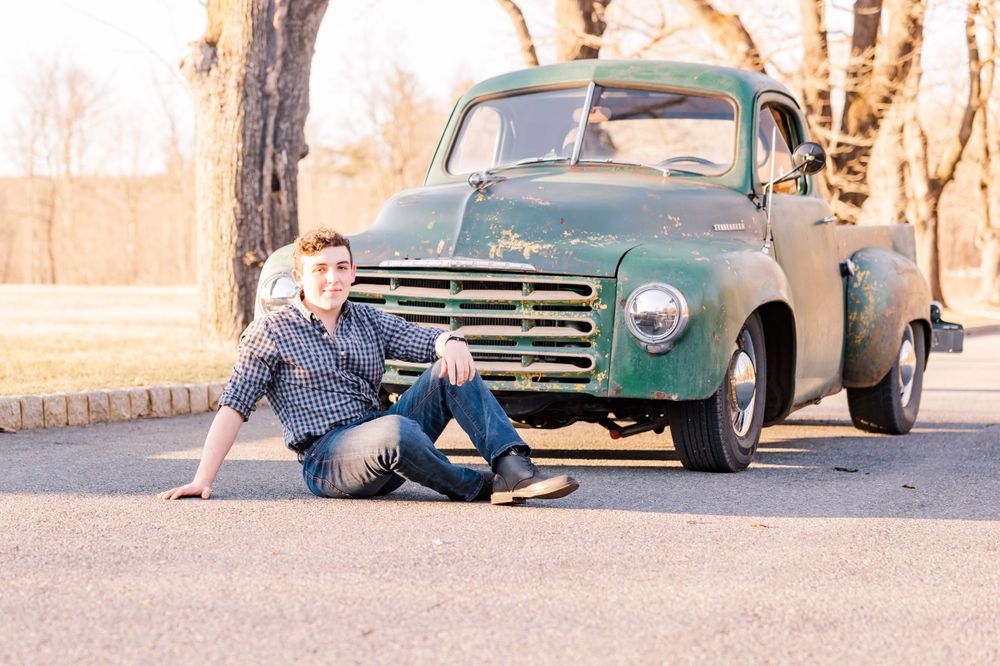 Person sitting on ground next to vintage green truck during golden hour.