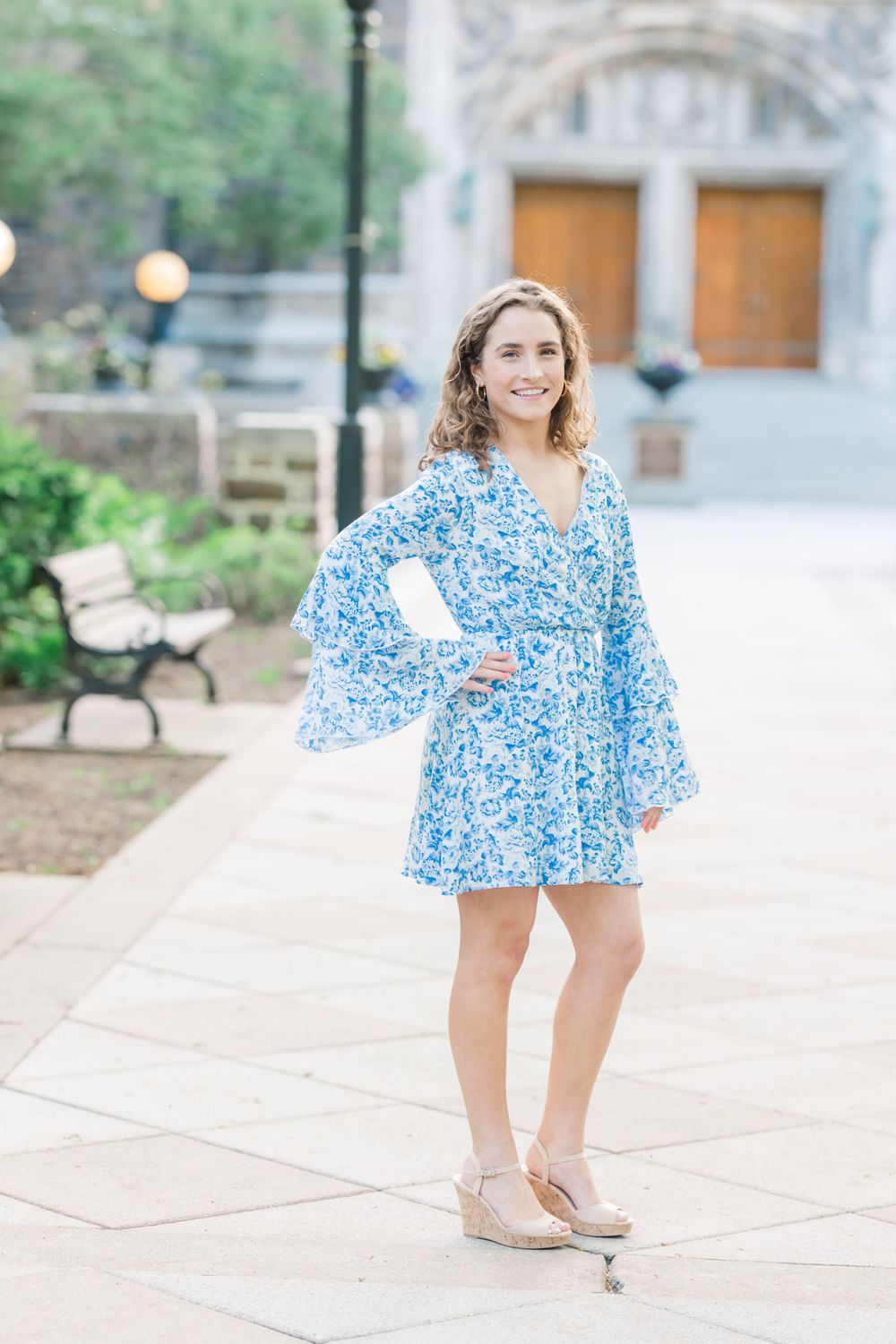 A person wearing a light blue floral dress stands on a stone walkway near benches.