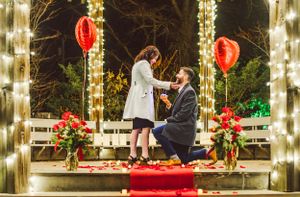 A romantic proposal scene at night with red balloons and twinkle lights decorating a wooden gazebo platform.  Brunswick, Maine.