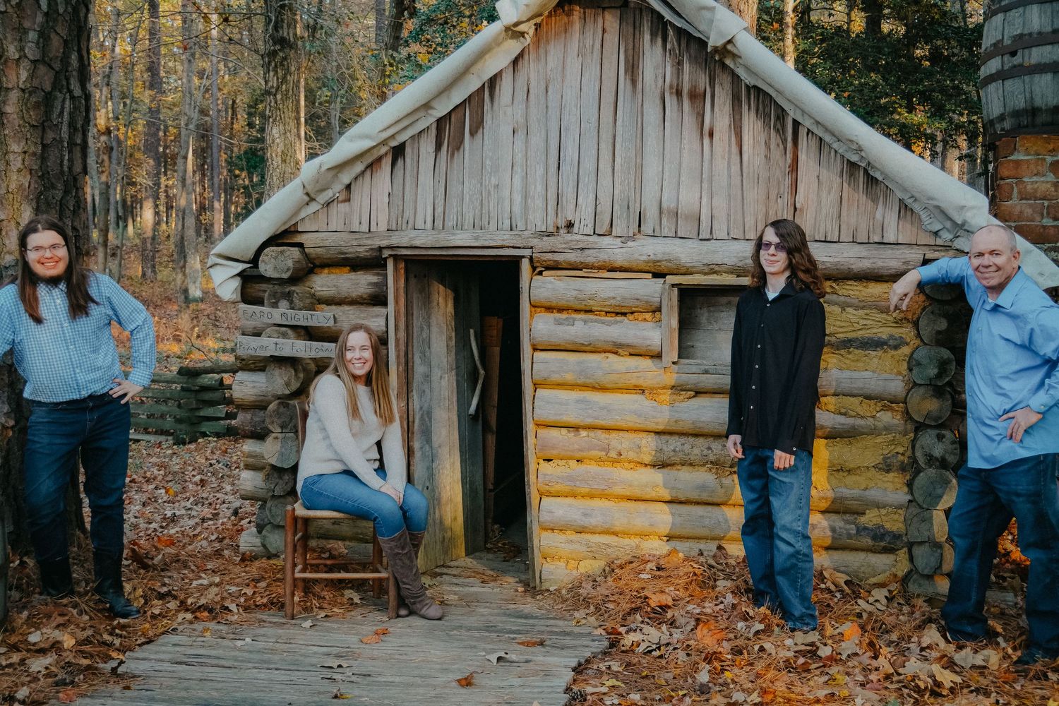 Group gathered around rustic log cabin in autumn forest setting.
