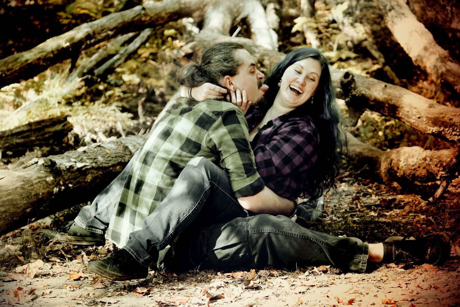 Artistic couple photo with two people laying on fallen logs in plaid shirts.