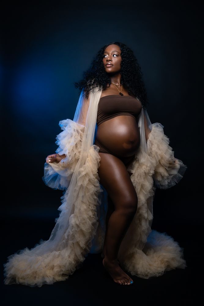Dramatic boudoir portrait with flowing tulle robe against dark background.