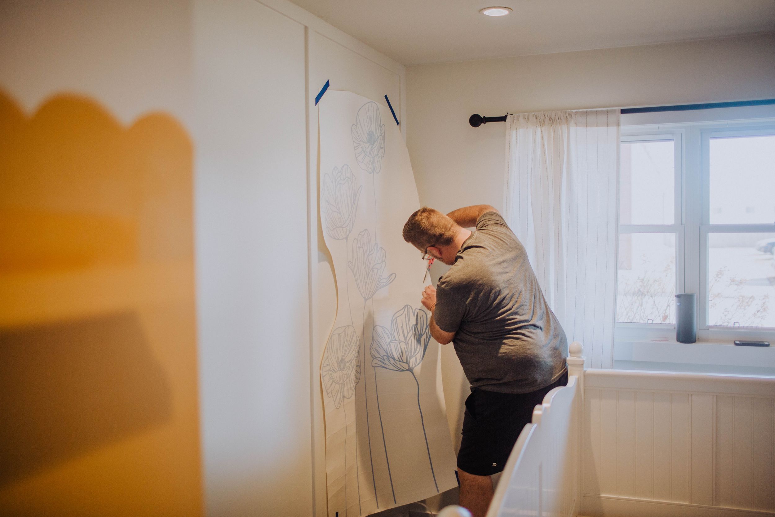Wall mural being sketched on white wall in room with natural lighting.