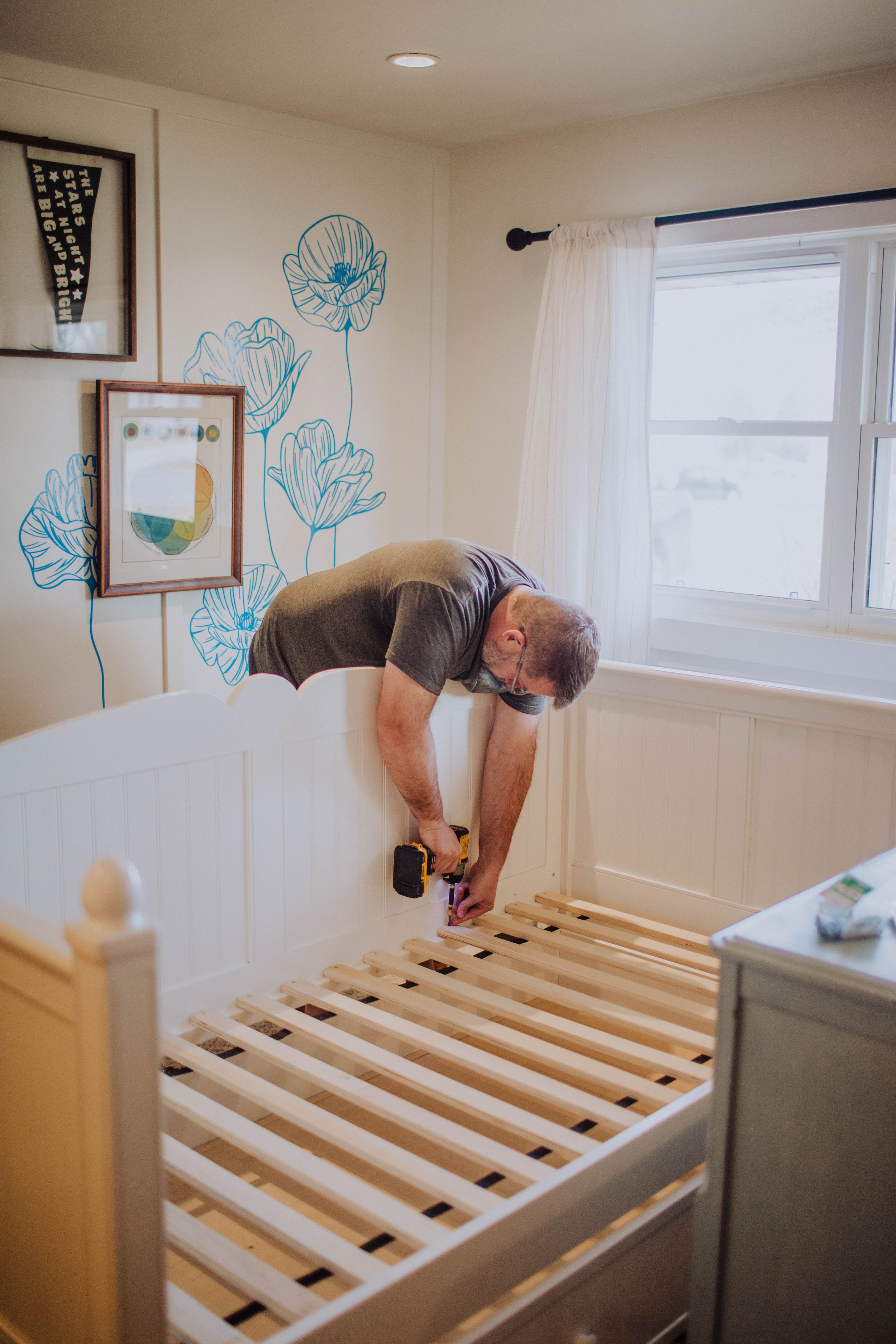 Assembly of wooden bed slats with blue floral wall art in background.