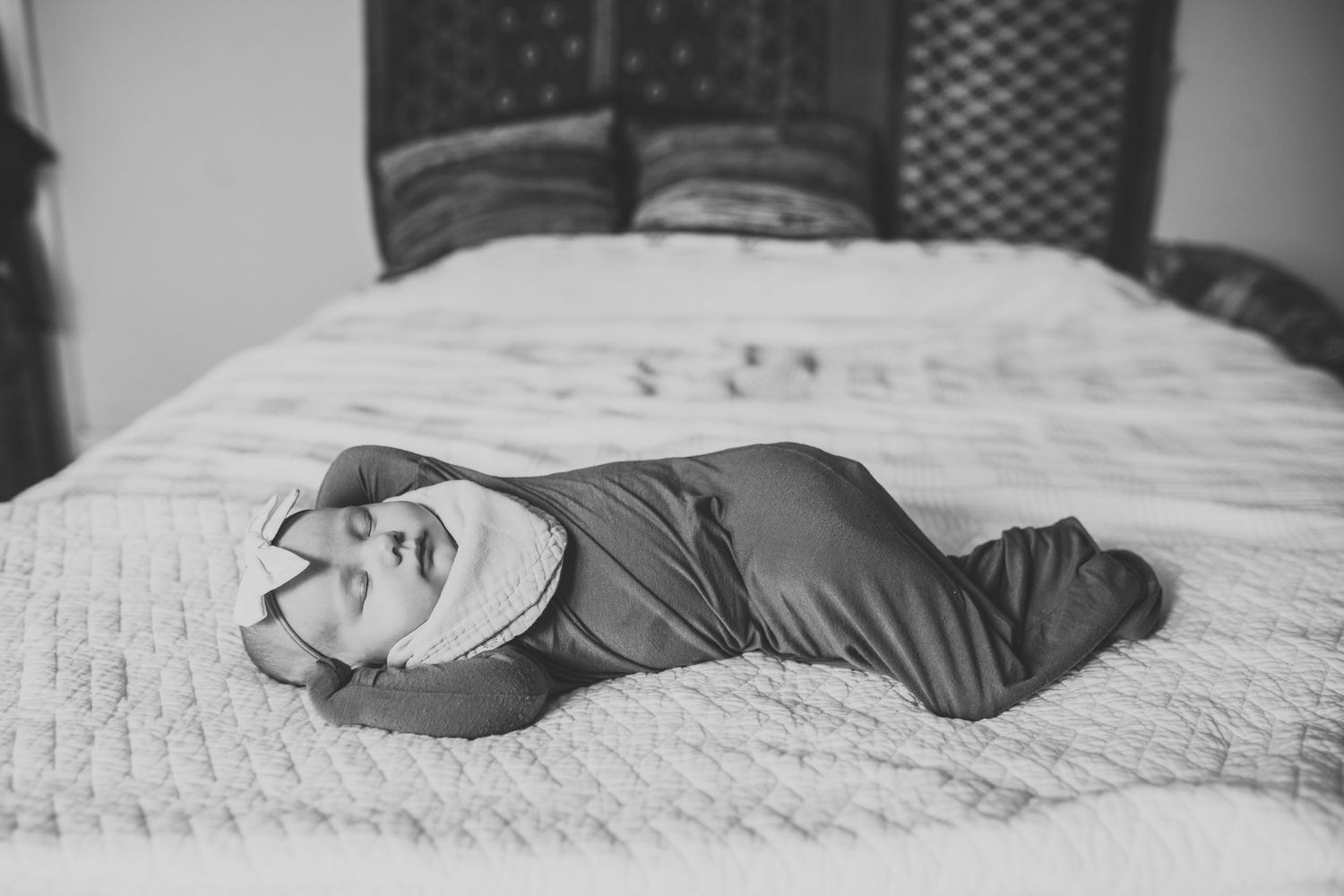 Little baby girl with a bow lies asleep on a bed with her arms up