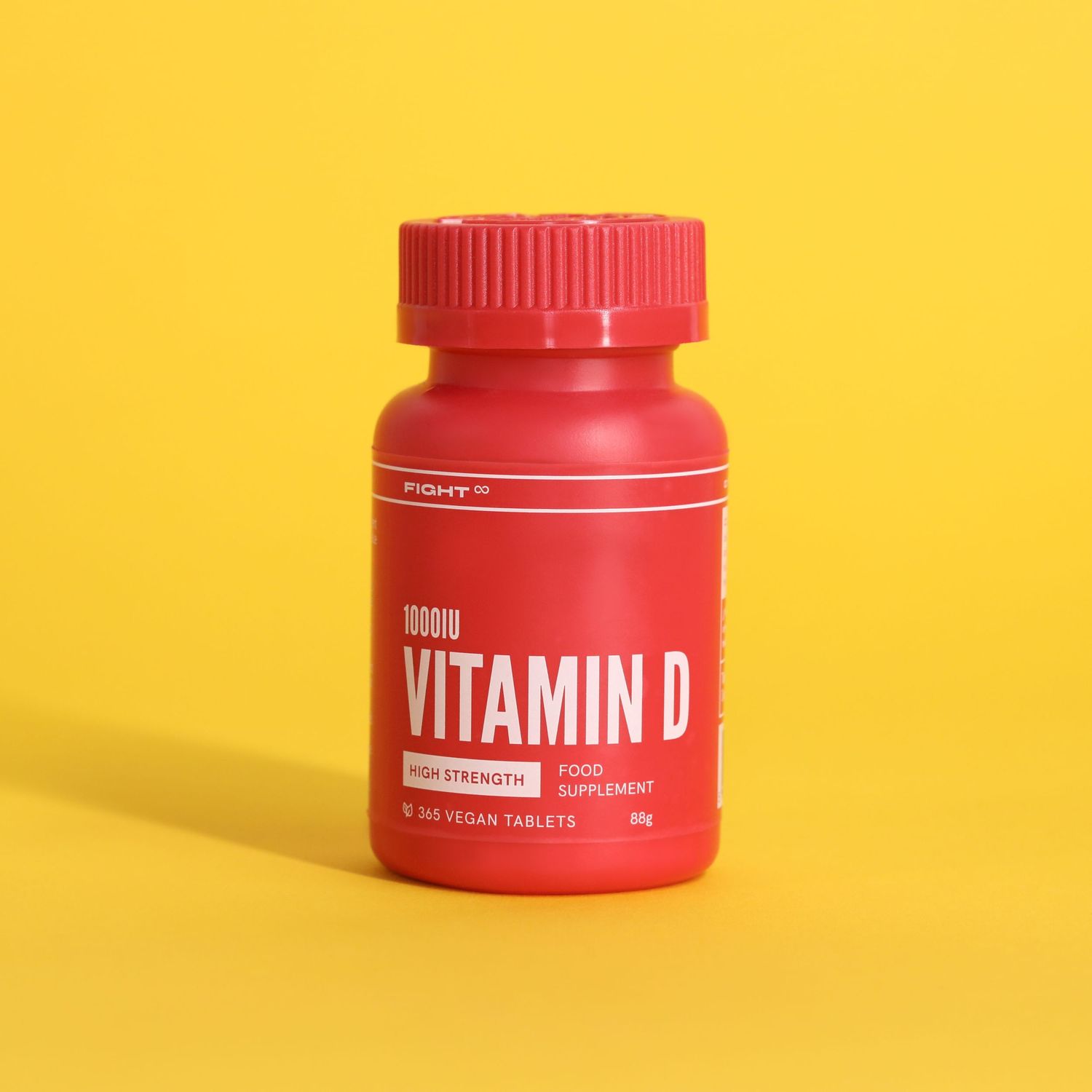 Red bottle of Vitamin D supplements against bright yellow background.