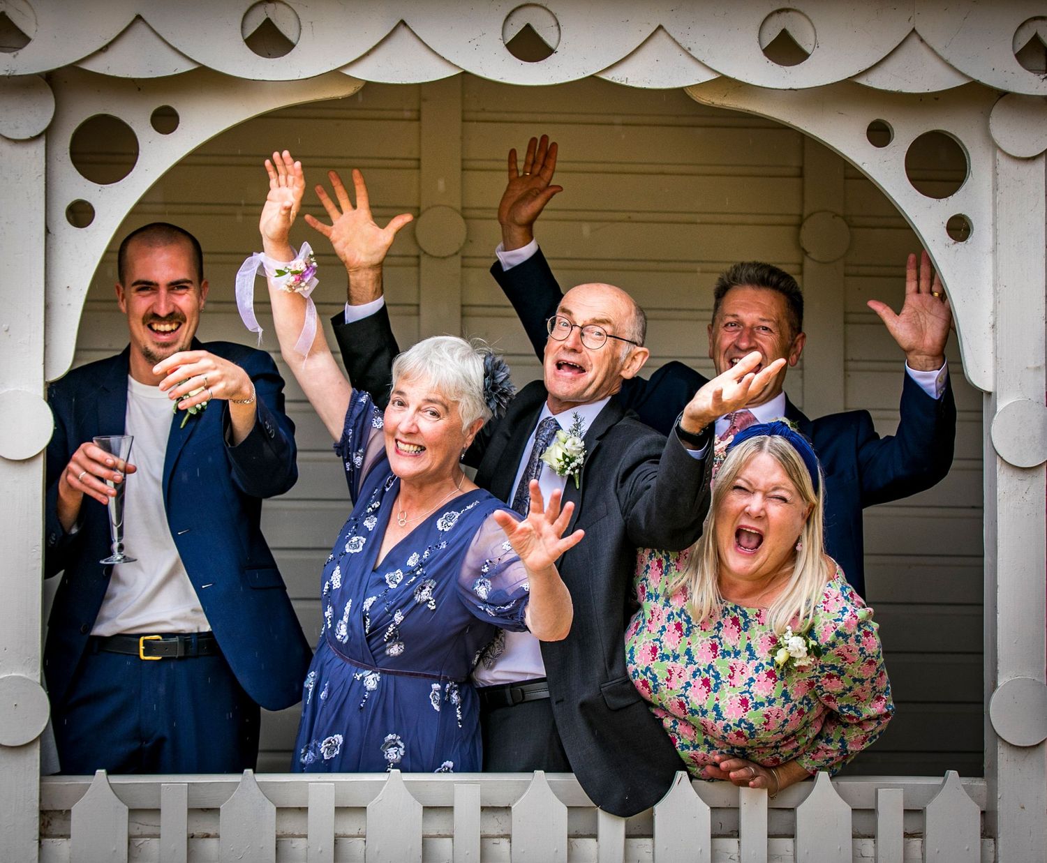 Joyful wedding guests waving and celebrating from a white gazebo.