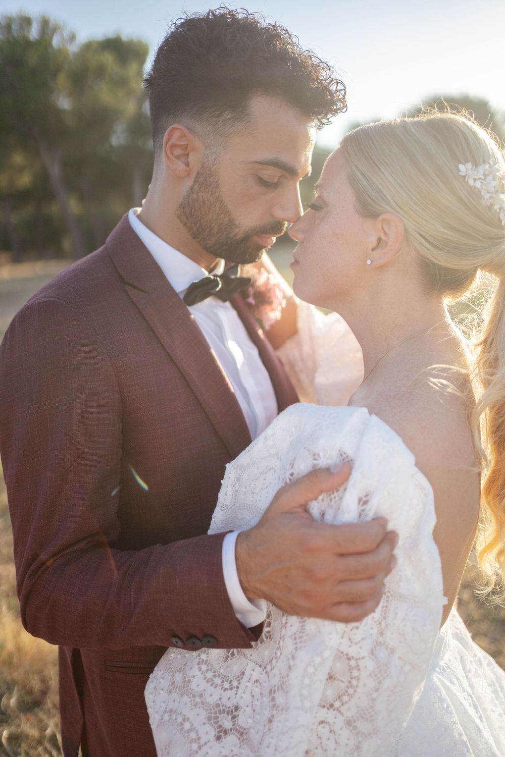 Romantic sunset portrait of newlyweds embracing in formal wedding attire.