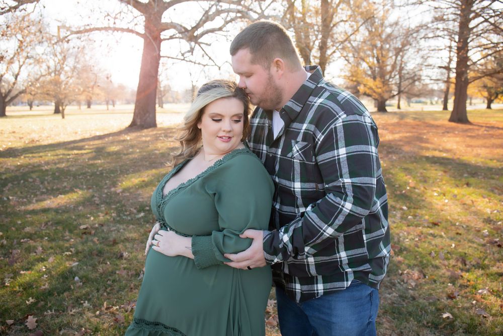 An affectionate couple poses together among fall trees during a maternity photoshoot.