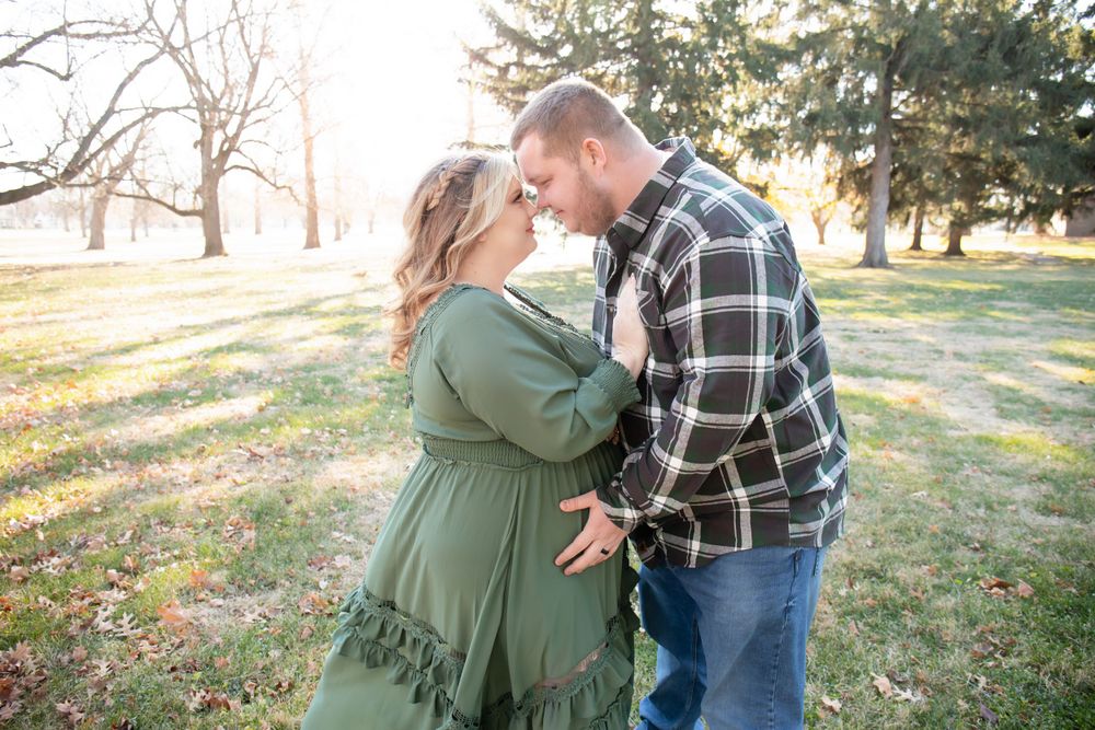 A romantic maternity photo of a couple sharing a moment in a fall park setting.