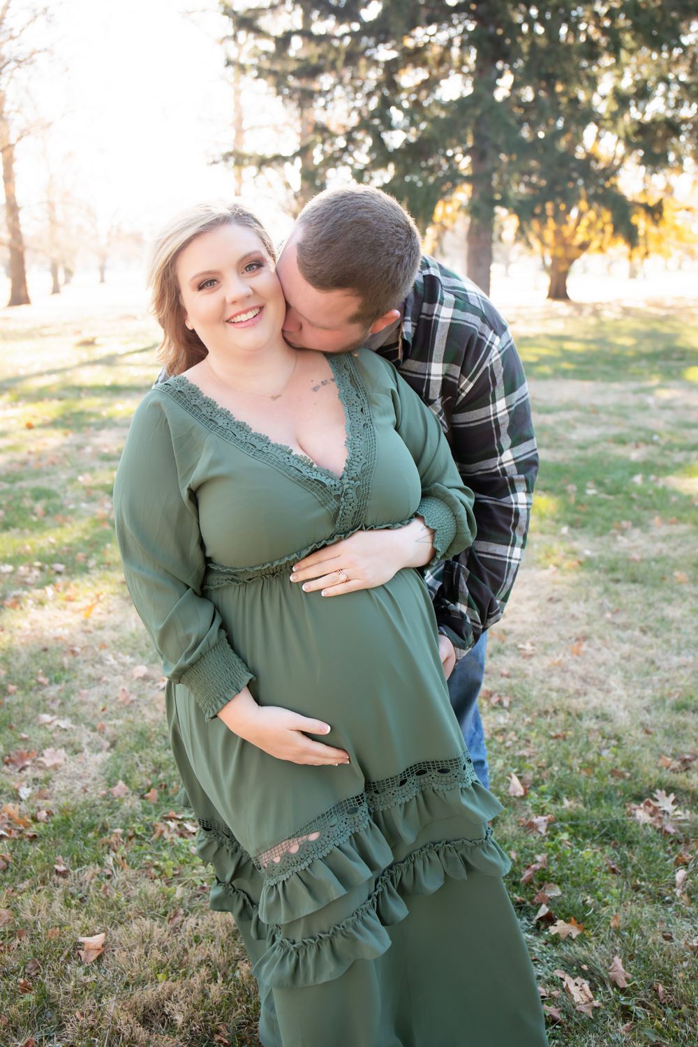 A maternity photoshoot featuring a couple in casual attire among autumn trees.