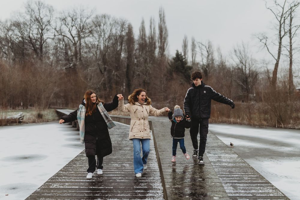 Family walking and holding hands while balancing on snowy boardwalk.