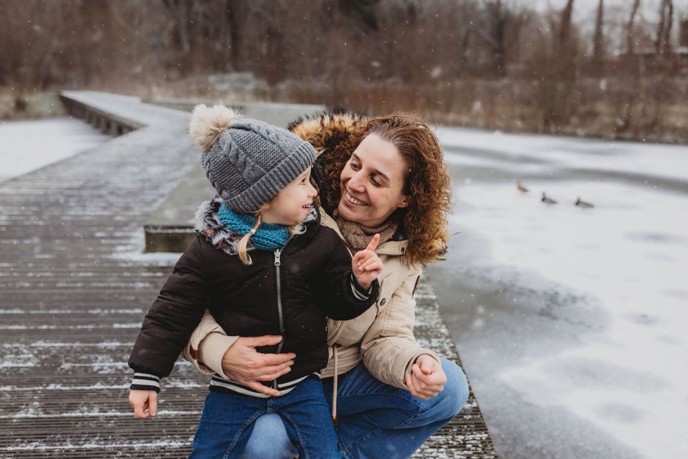 Tender winter moment shared between two people on a wooden boardwalk by frozen water.