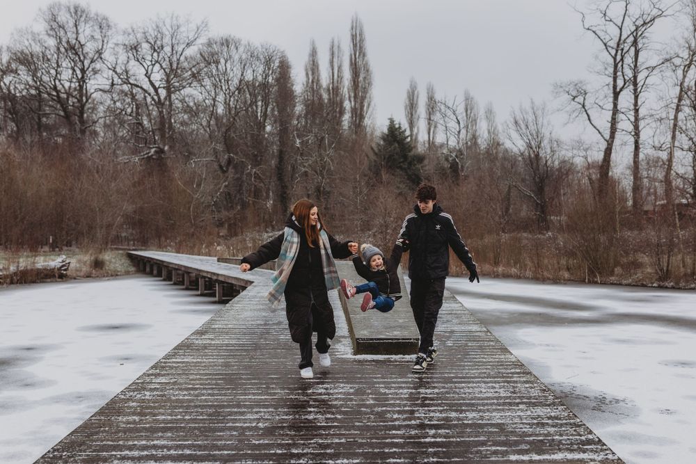 Family running together playfully on a snowy wooden boardwalk.