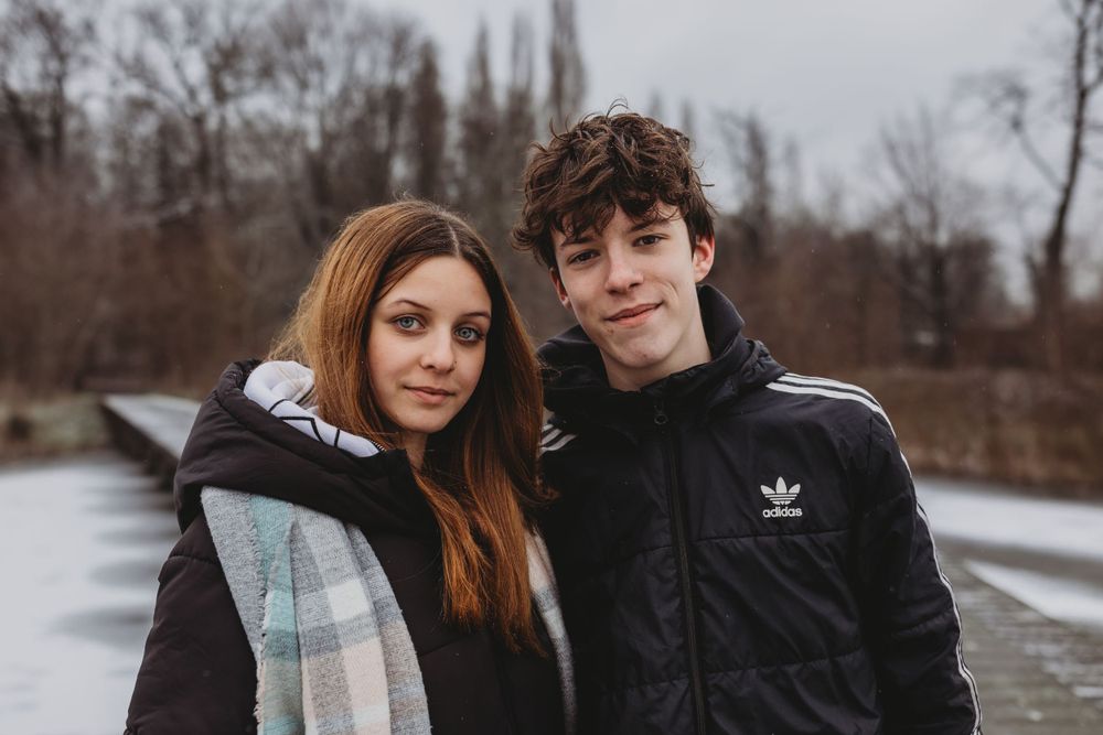 Winter portrait of two people on wooden boardwalk with bare trees in background.