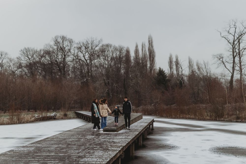 People walking along a snowy wooden boardwalk surrounded by bare winter trees.