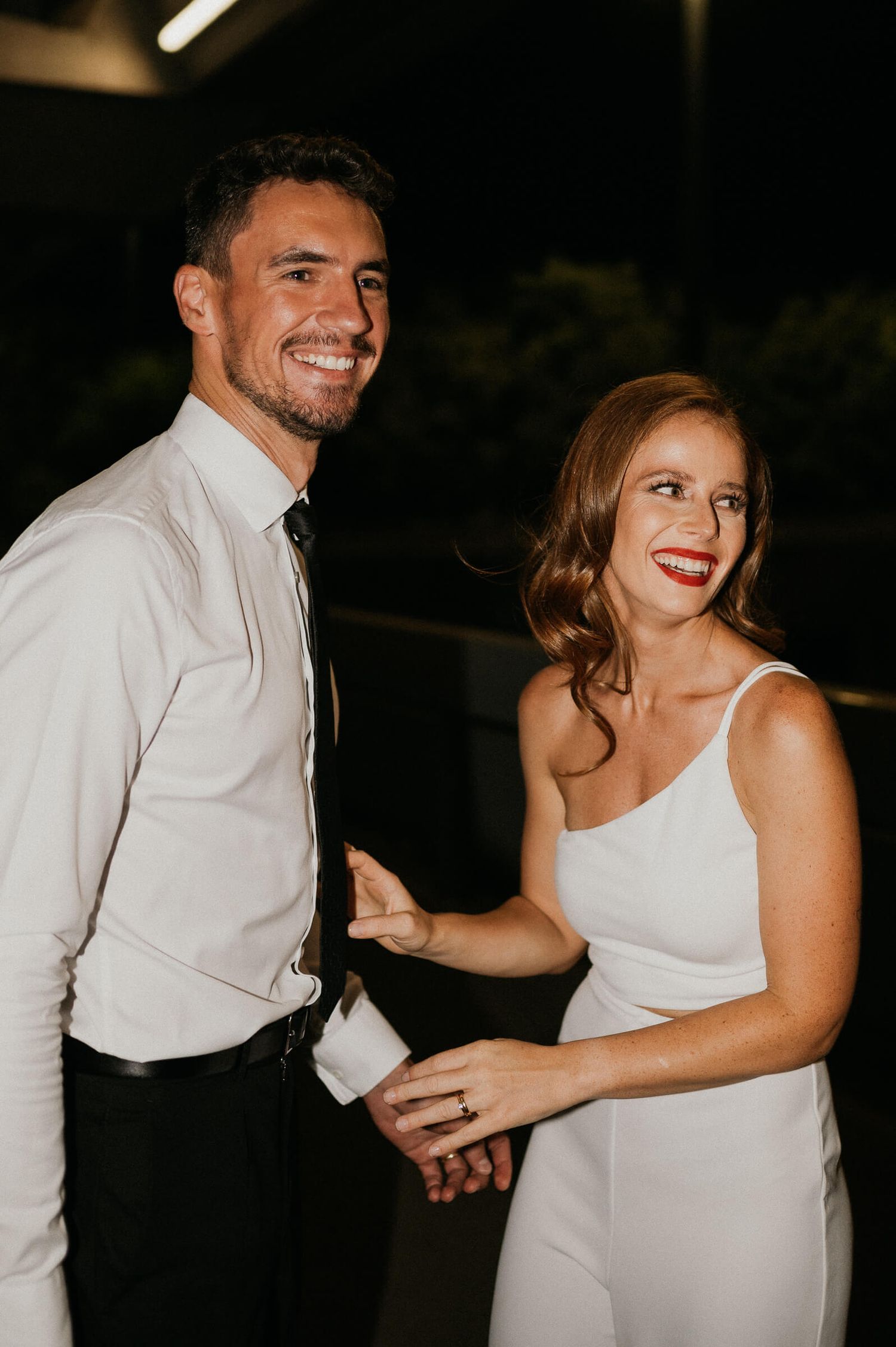 A happy couple in formal attire shares a candid laughing moment during an evening celebration.