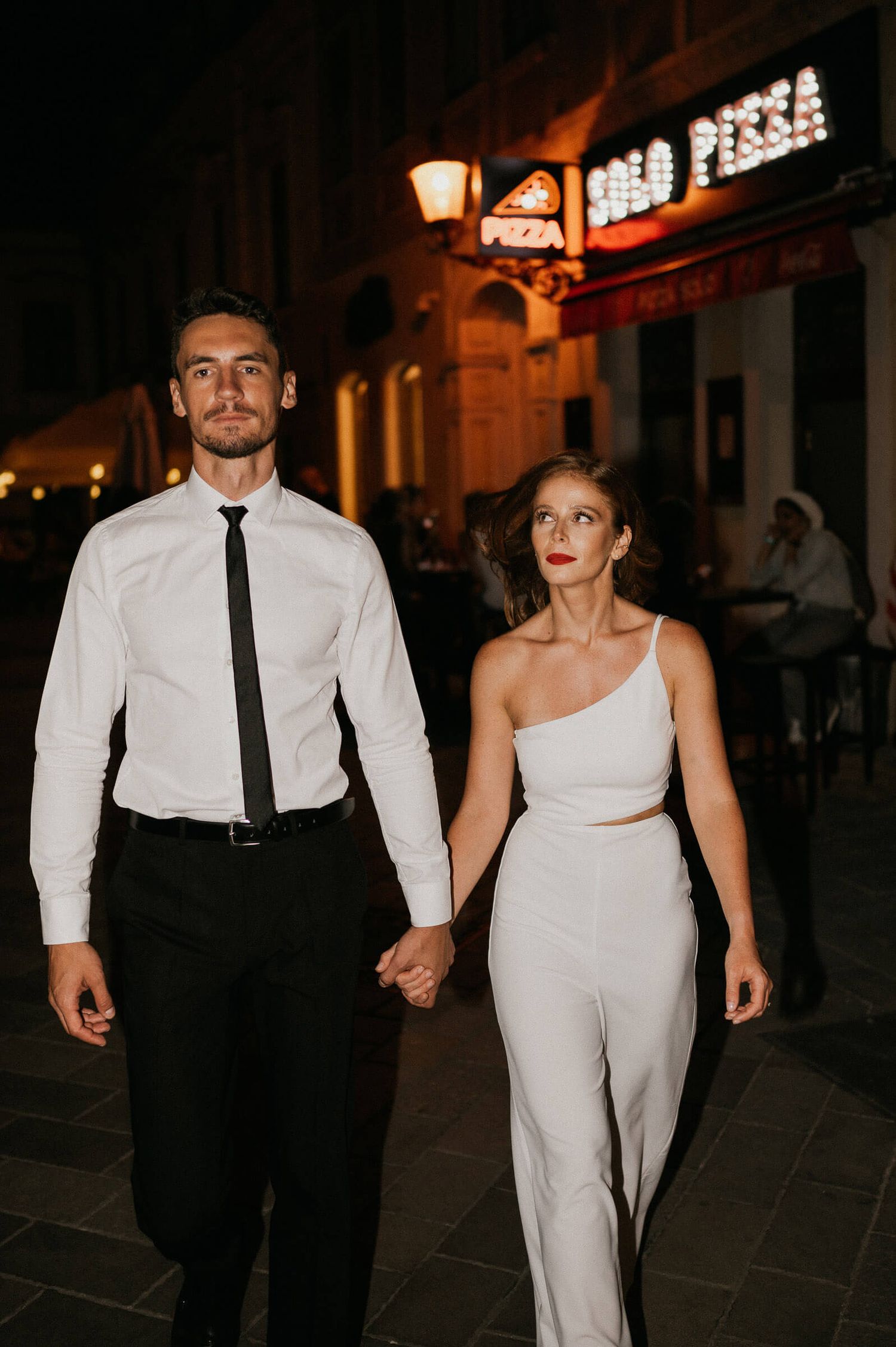 A couple in coordinated black and white outfits walking together at night under city lights.
