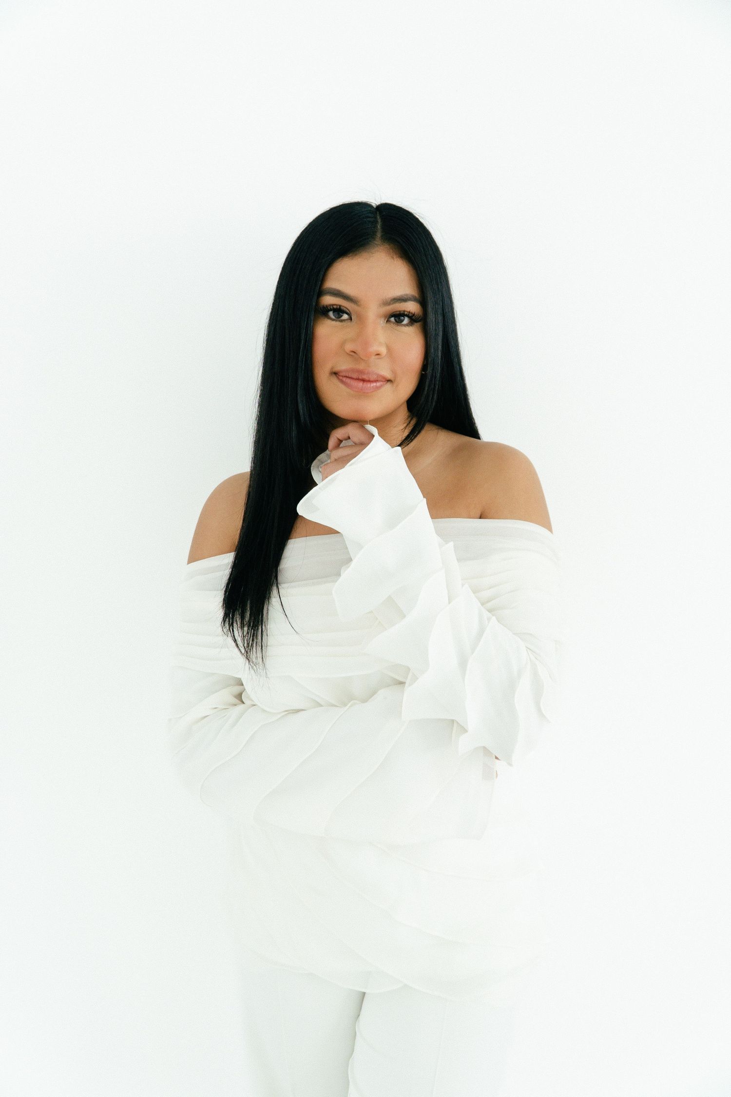 Woman in white off-shoulder sweater poses against white background.