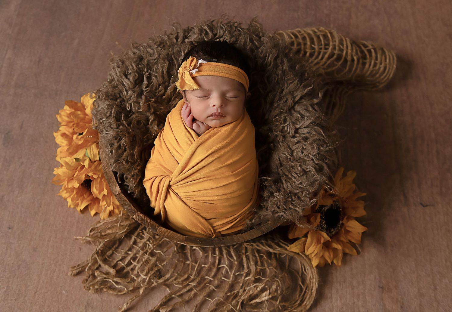 Newborn baby nestled in yellow wrap with sunflowers during professional photo shoot.
