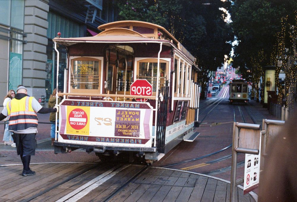 Classic San Francisco cable car on a steep city street with a worker in high-vis vest.