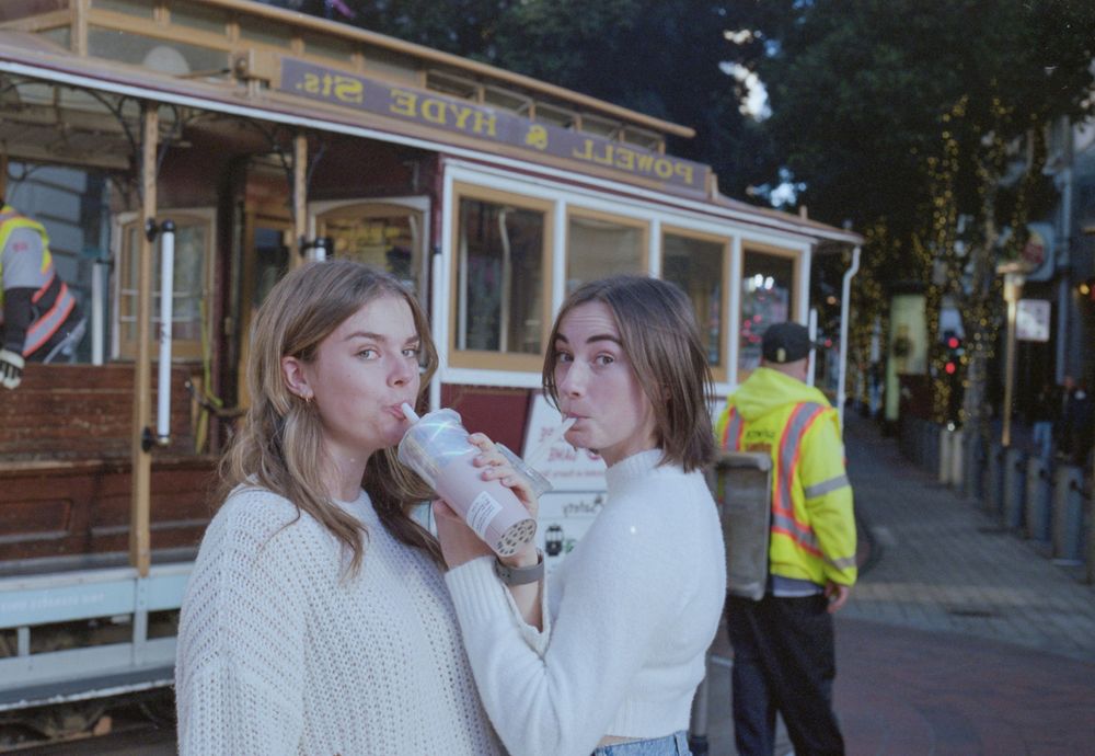 Friends sharing drinks in front of a vintage San Francisco cable car.