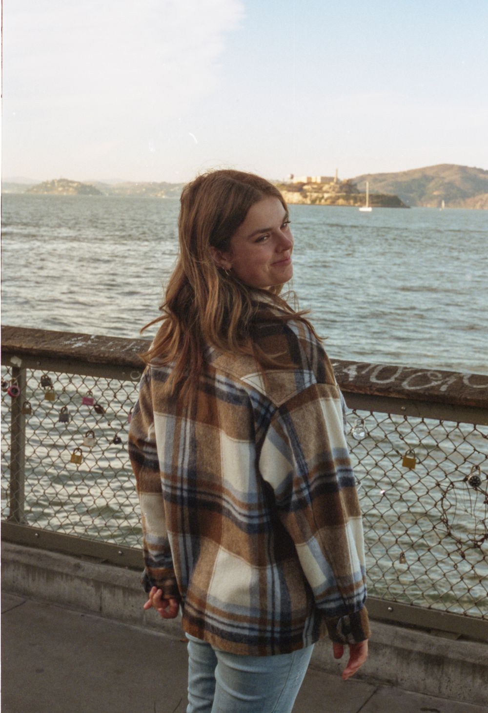 People enjoying scenic views of Alcatraz Island from a waterfront railing in San Francisco on a sunny day.
