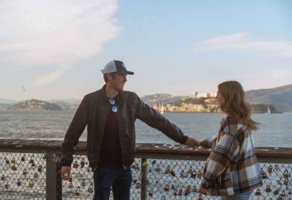 Visitors enjoying a scenic moment at the San Francisco pier with Alcatraz Island in the distance.