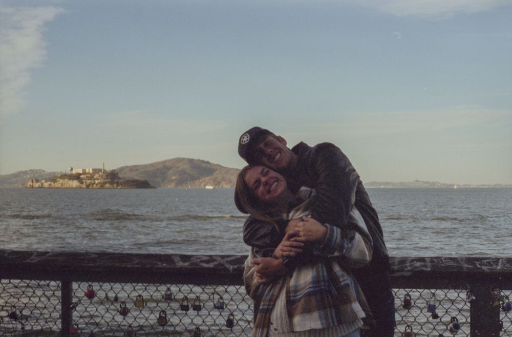 Warm embrace shared between friends at San Francisco's pier with the bay in the background.