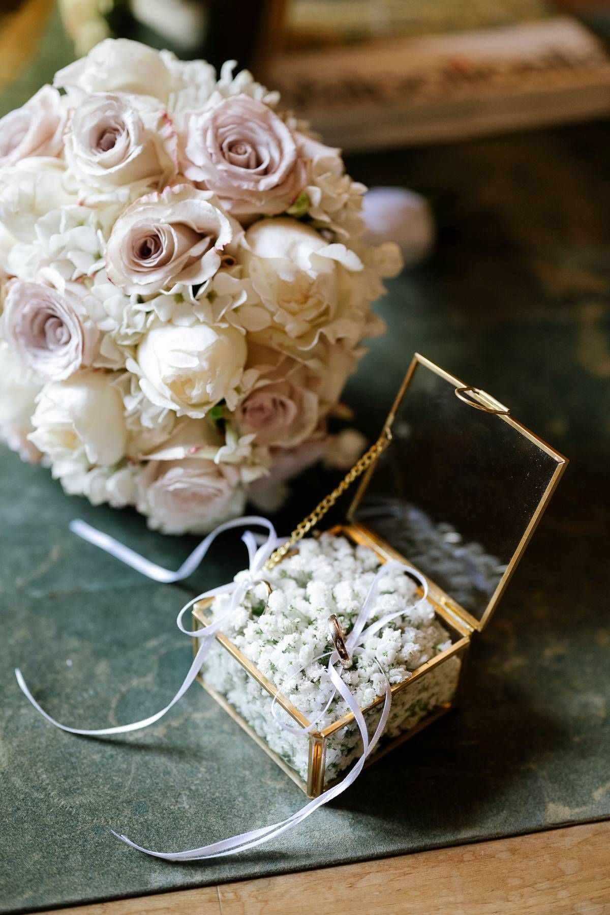 Elegant bridal bouquet of blush pink and white roses next to a gold glass jewelry box.