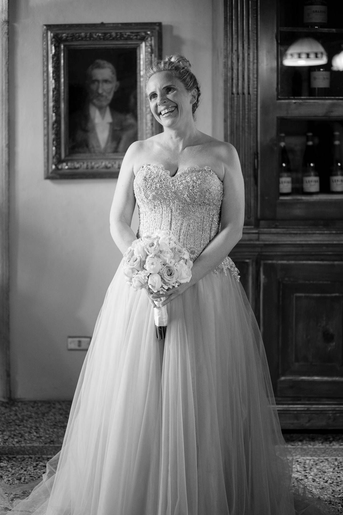 Black and white portrait of someone in a wedding gown holding a bouquet and smiling brightly.