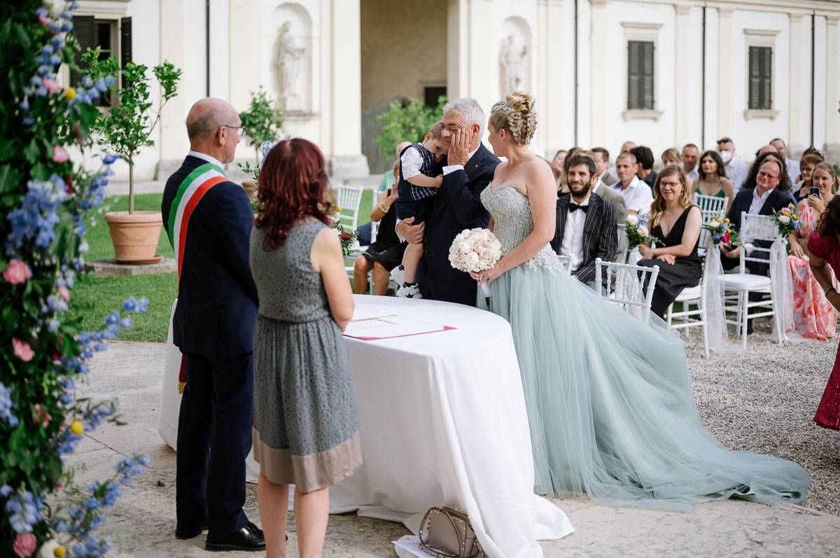 Wedding guests watch as couple signs documents at elegant outdoor ceremony with light blue gown.