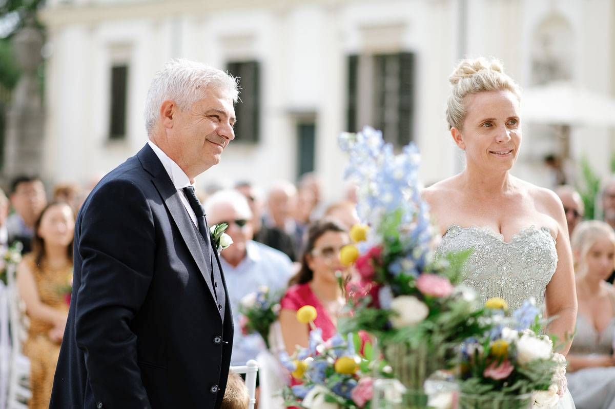 Elegant outdoor wedding ceremony with floral arrangements and classical architecture in background.
