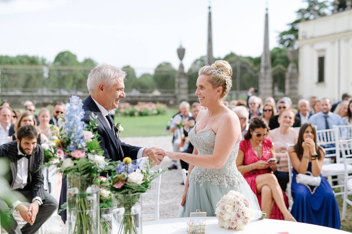 Emotional ceremony moment during outdoor wedding with floral arrangements and guests looking on.