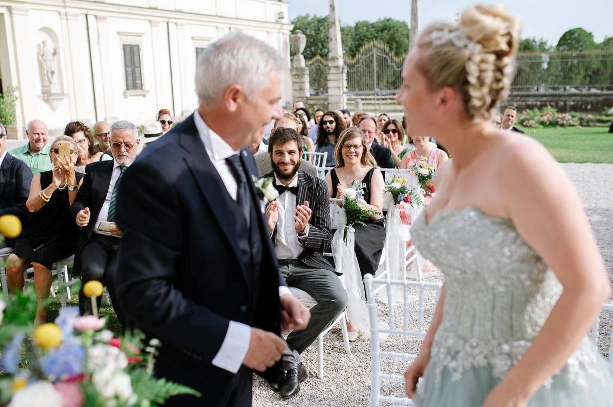 A joyful moment during an outdoor wedding ceremony with guests watching in the background.