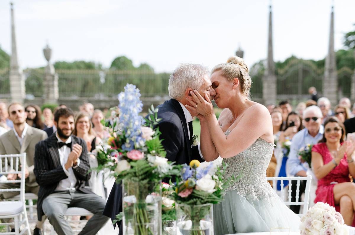 An emotional wedding ceremony moment captured outdoors with guests applauding.