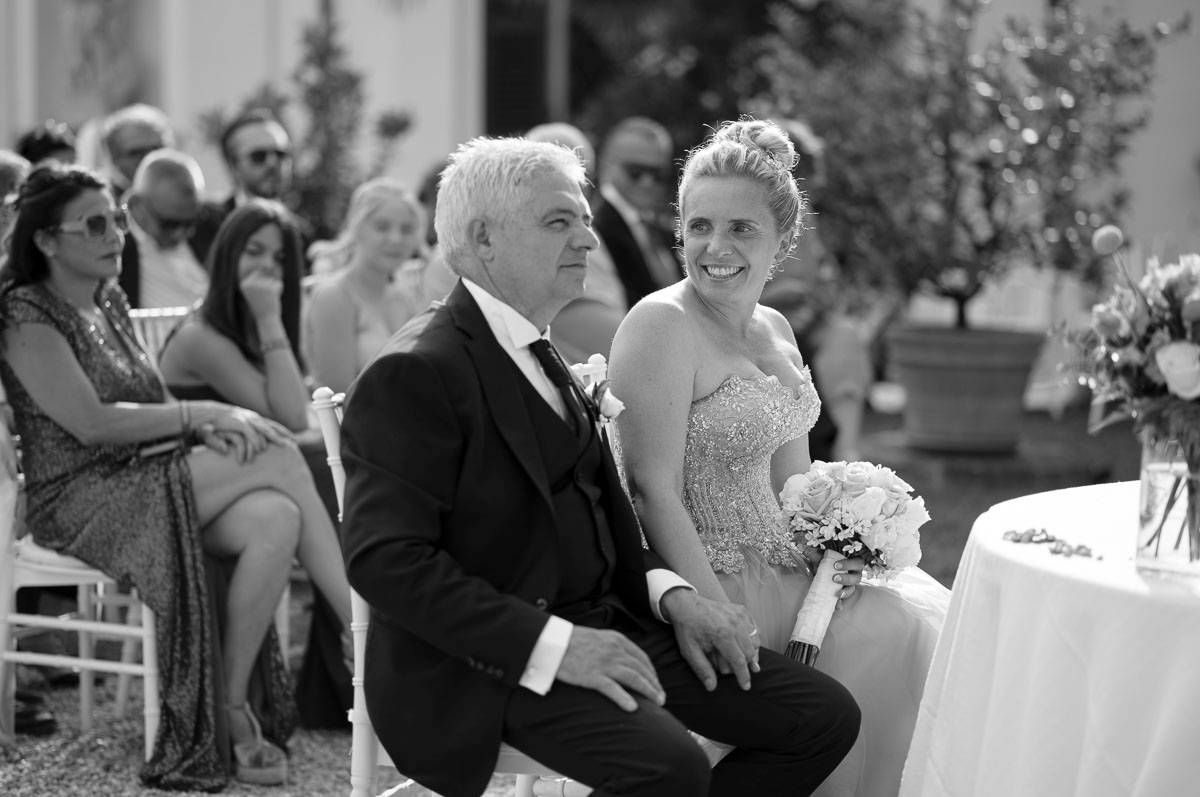 Black and white photo of guests seated at an outdoor wedding celebration with floral decorations.