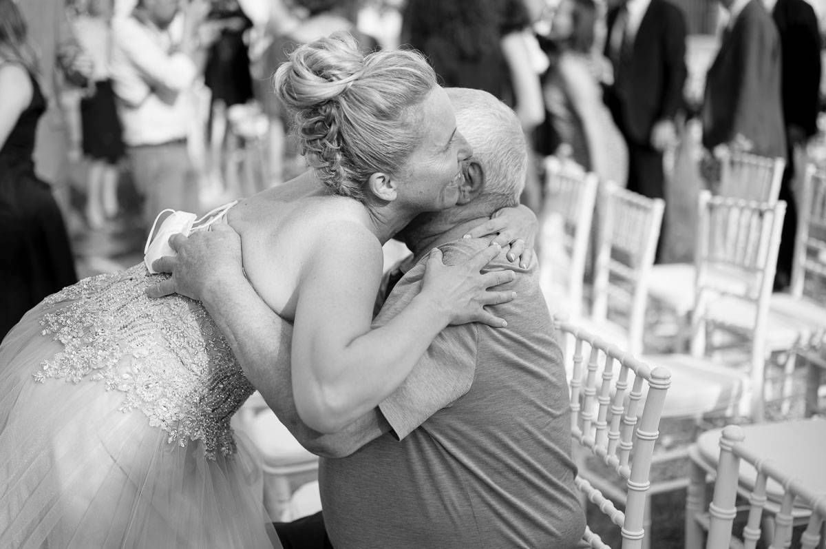 Bride in sparkly dress shares emotional embrace during wedding reception.