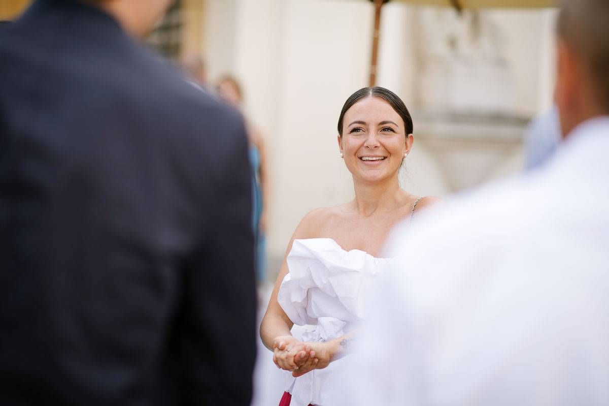Bride in white strapless gown smiles radiantly during wedding ceremony.