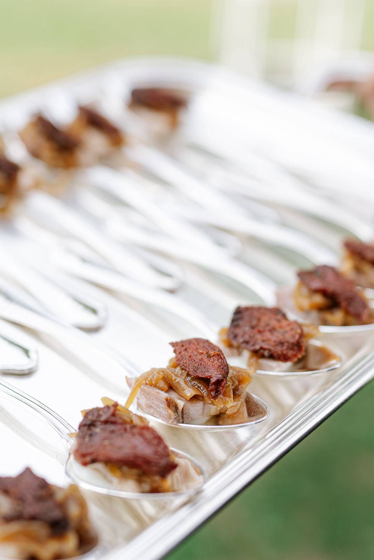 Small bites of caramelized meat appetizers served on elegant white spoons at an upscale event.
