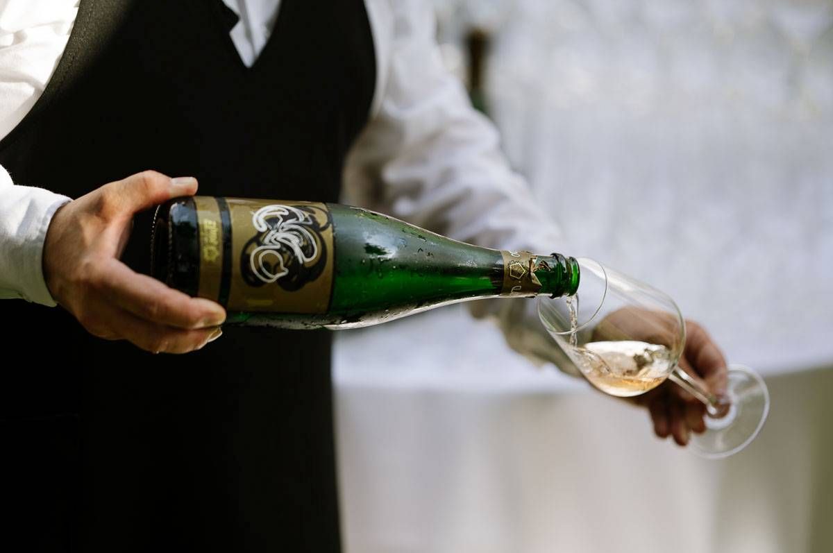 Server pouring champagne from a green bottle into a glass flute at an elegant event.