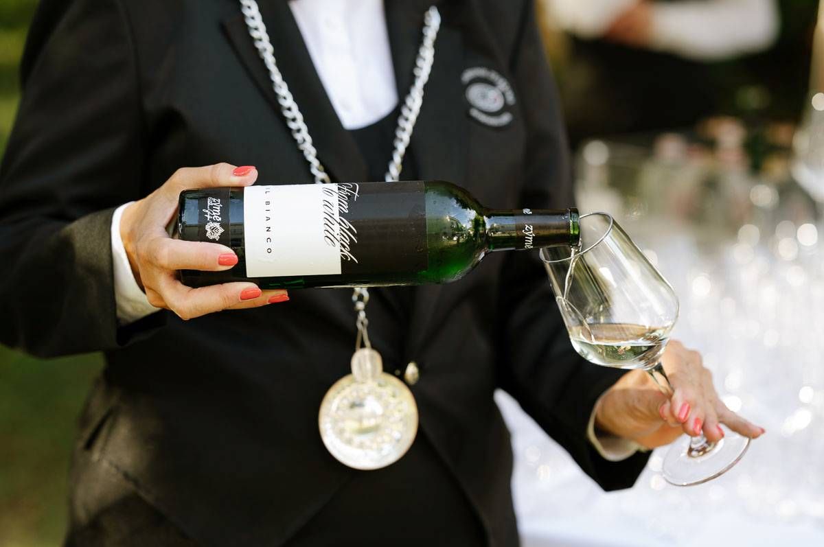 Server pouring wine into crystal glass at outdoor event.