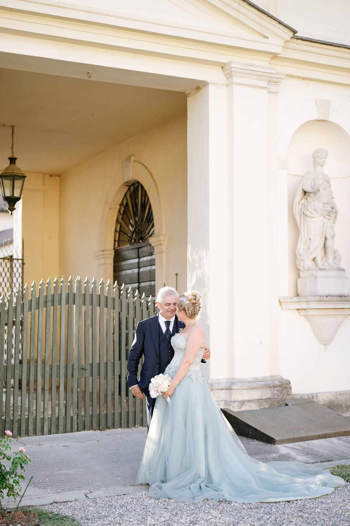 Couple posing by classical architecture entrance with ornate gate and statue.